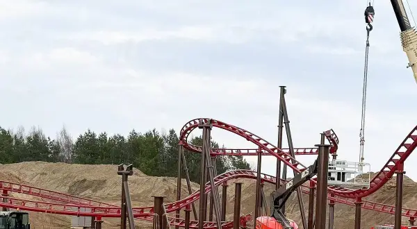 Budowa **Hosso Park Rozrywki** trwa. Czerwone tory kolejki górskiej wznoszą się nad placem budowy, gdzie pracują dźwigi i koparki.