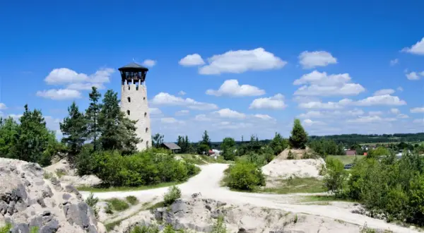 Kamienna wieża widokowa Józefów góruje nad piaszczystym krajobrazem, otoczona zielenią i błękitnym niebem z chmurami.