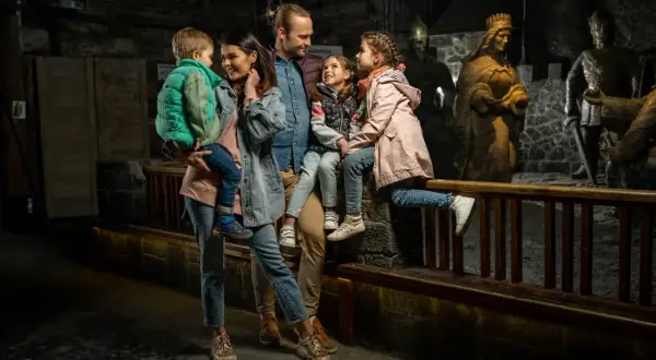 Rodzina zwiedza kopalnię soli w Wieliczce. Dzieci z rodzicami podziwiają solne rzeźby królów i rycerzy.