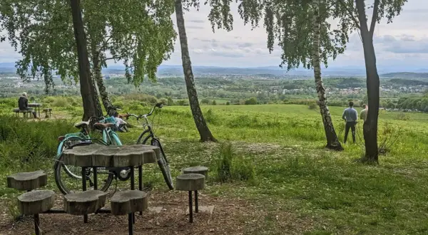 Idealny punkt widokowy Kraków. Dwa rowery, drewniany stolik i ławki czekają na turystów. W oddali rozciąga się malowniczy krajobraz.