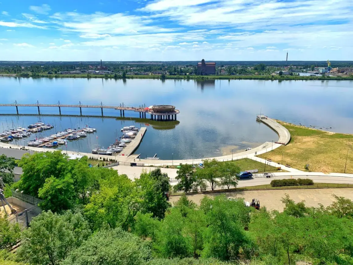 Płock co zobaczyć: malownicza marina z żaglówkami, nowoczesny deptak nad Wisłą i industrialne krajobrazy w tle.