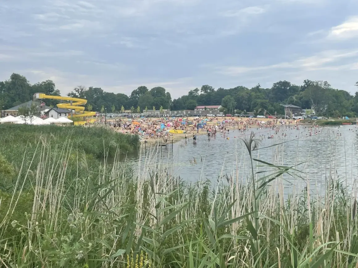Tłum ludzi wypoczywa nad wodą na plaży w Lisowicach. W oddali widać żółtą zjeżdżalnię wodną.