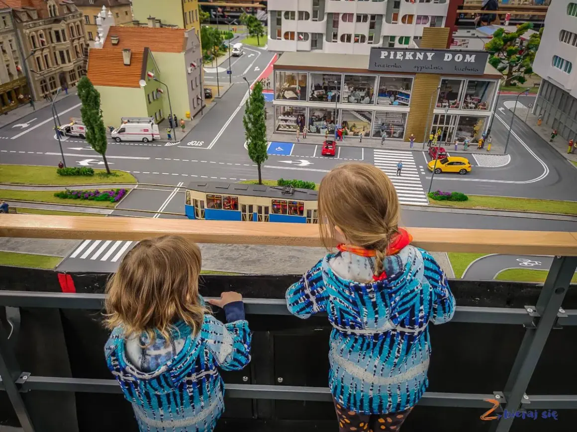 Dwie dziewczynki oglądają miniaturową ulicę z tramwajem i budynkami w parku miniatur Wrocław.