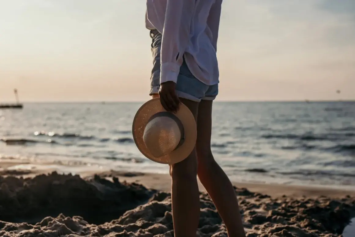Spacer po plaży w Kołobrzegu. Słońce zachodzi nad morzem, a w dłoni trzymam słomkowy kapelusz.