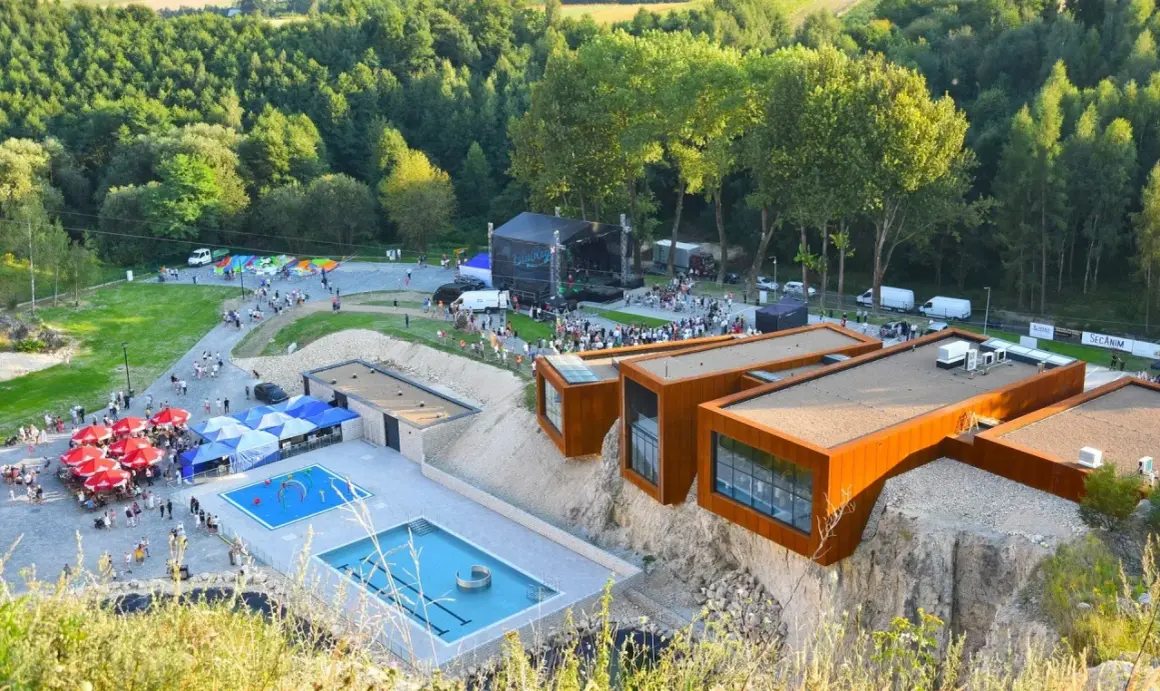 Ulinapark tętni życiem: koncert na scenie, baseny, punkty gastronomiczne i nowoczesne budynki na skale.