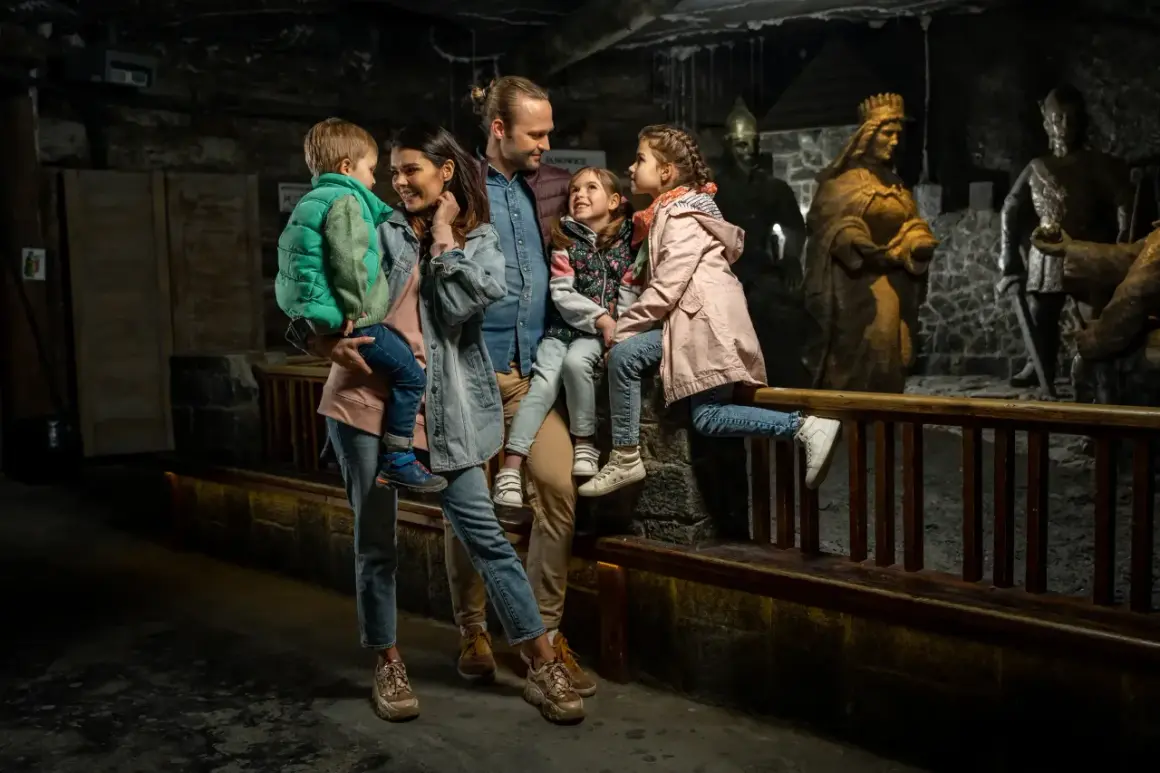 Rodzina zwiedza kopalnię soli w Wieliczce. Dzieci z rodzicami podziwiają solne rzeźby królów i rycerzy.