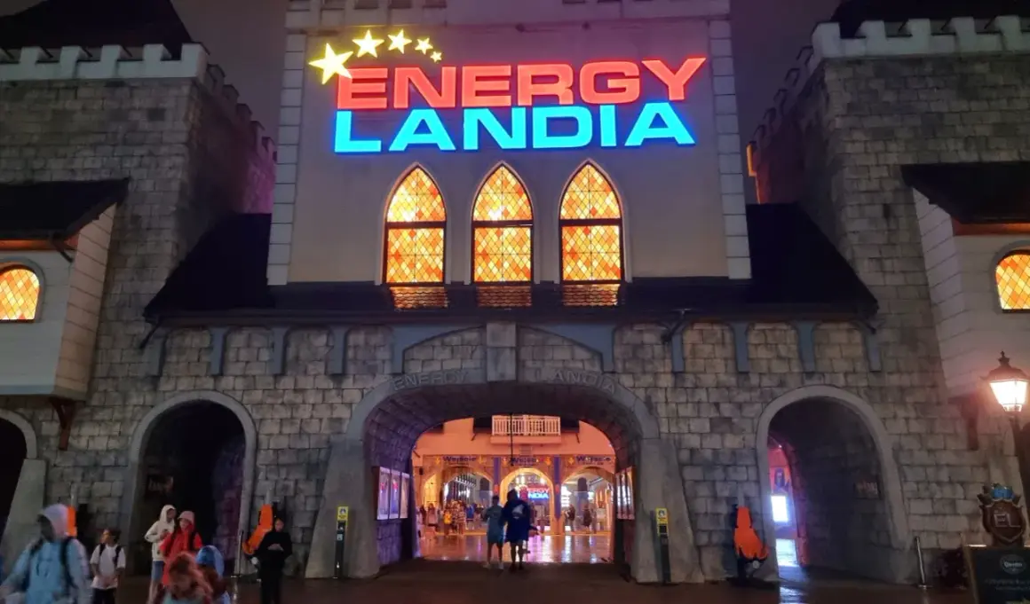 Wejście do Energylandii nocą, mimo deszczu, widać ludzi wchodzących pod łukiem.