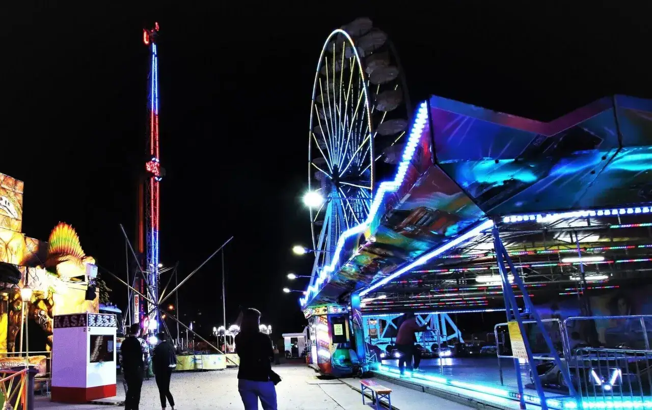 Nocny park rozrywki we Wrocławiu. Widać diabelski młyn, wieżę swobodnego spadania i kolorowe światła.