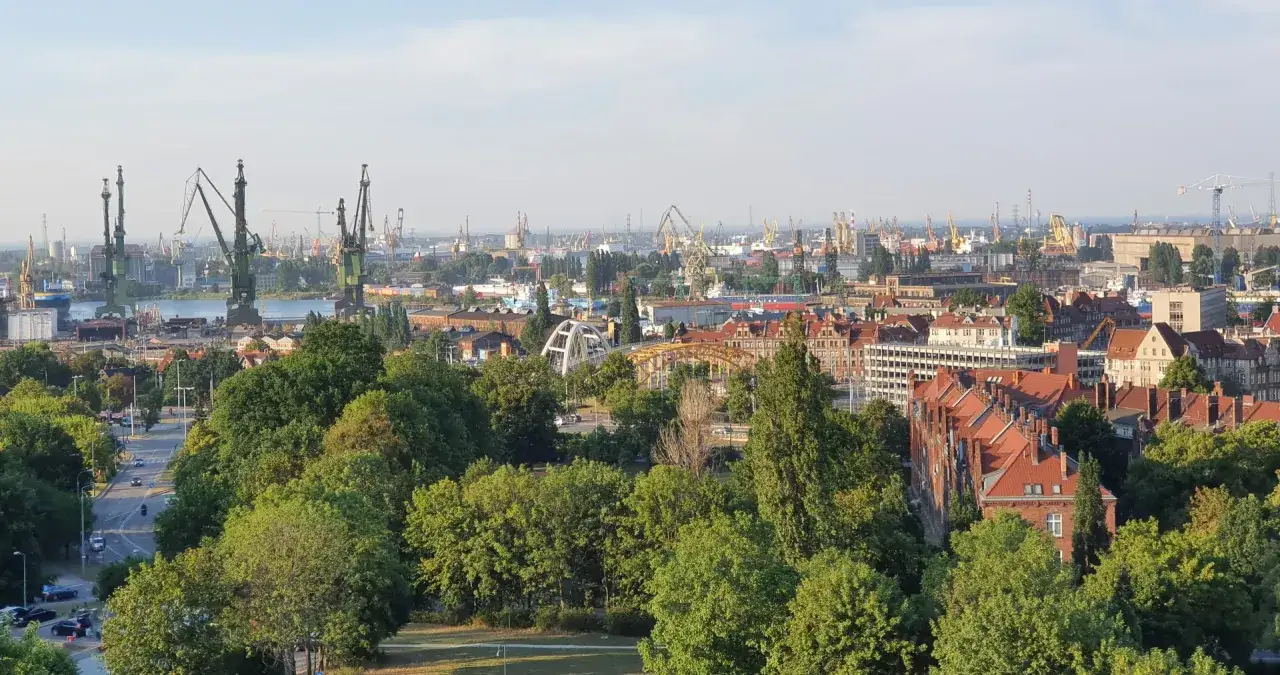 Widok z punktu widokowego Gdańsk na stocznię, portowe dźwigi i zabudowania miejskie.