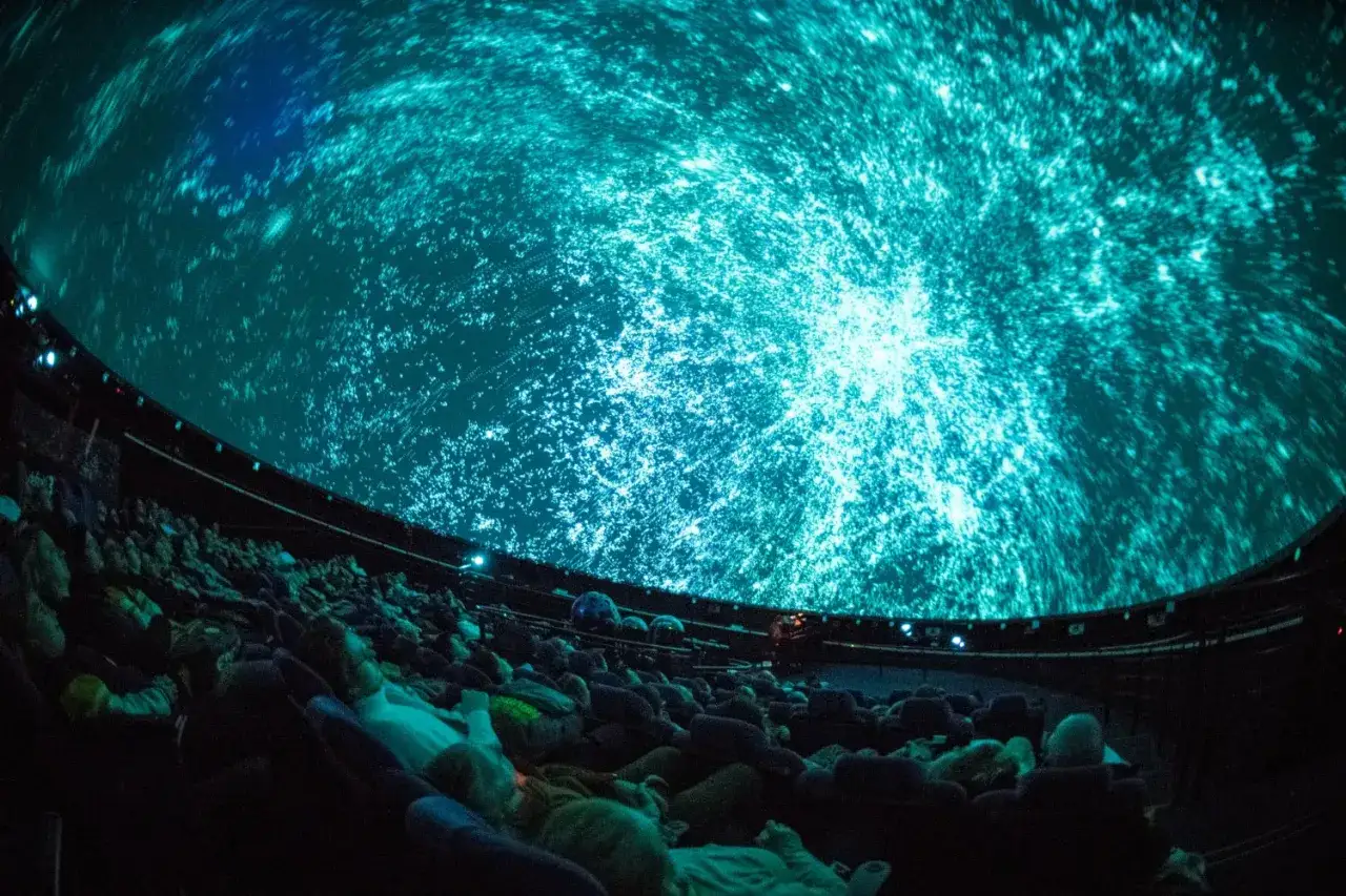 Widownia w planetarium Warszawa podziwia wirujący kosmos na kopule.