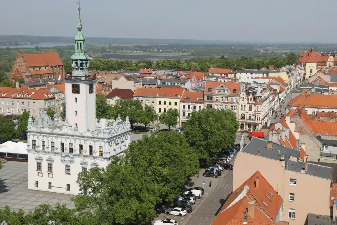 Widok na rynek w Chełmnie, z ratuszem i wieżą zegarową. W tle kamienice i zieleń, tworzące urokliwe chełmno atrakcje.