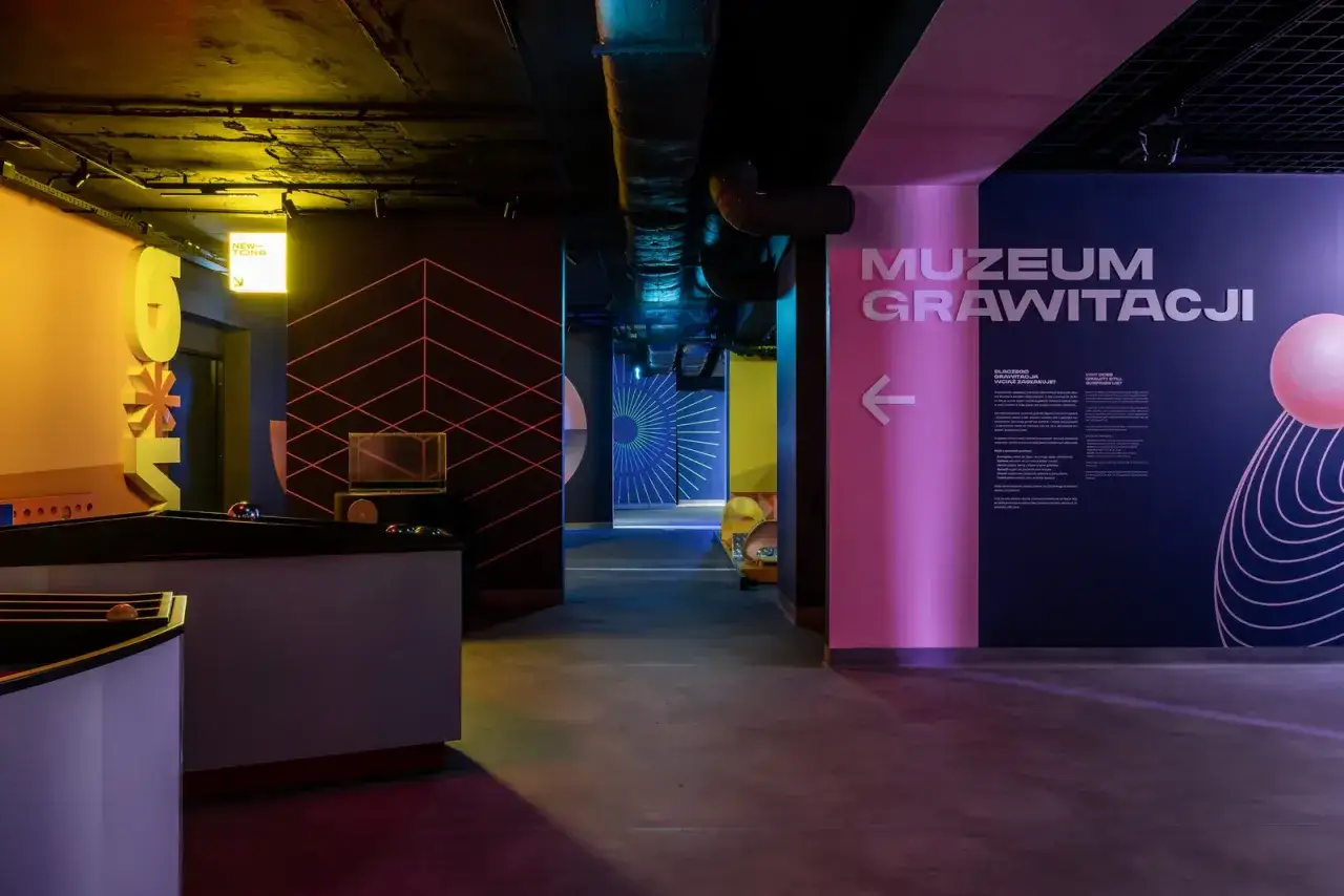 Kolorowe ściany i instalacje zapraszają do Muzeum Grawitacji. Widać tu tablice informacyjne i elementy interaktywne.