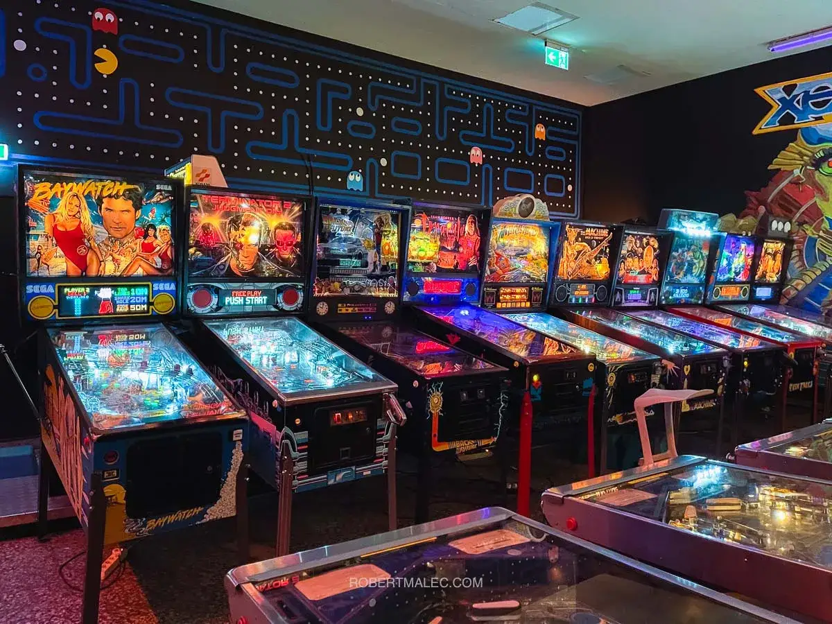 Rząd automatów do gry w pinball w krakowskim muzeum gier. Ściana ozdobiona motywem z Pac-Mana.