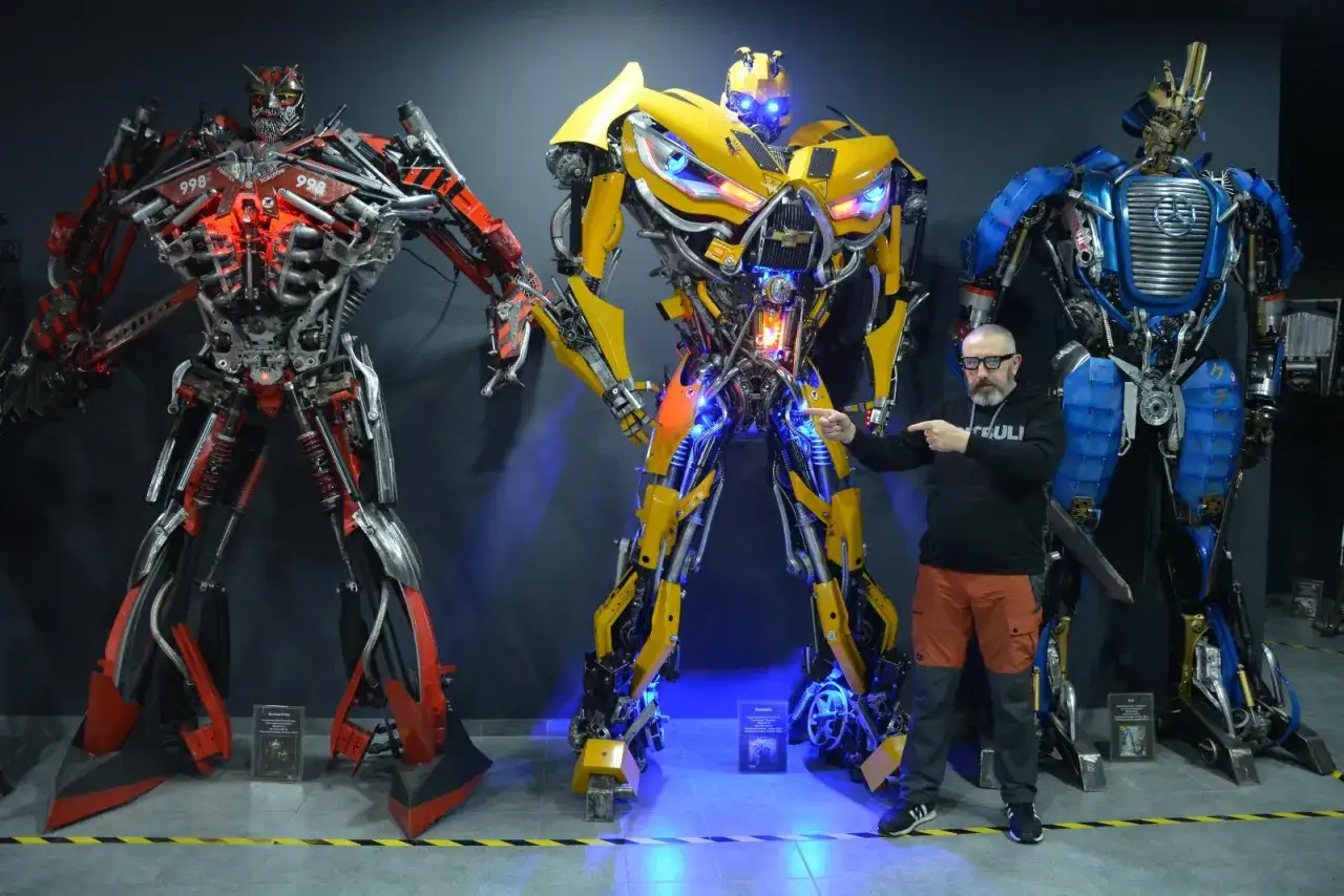 W muzeum robotów Moszna zobaczysz imponujące figury Transformerów. Mężczyzna stoi między czerwonym, żółtym i niebieskim robotem.