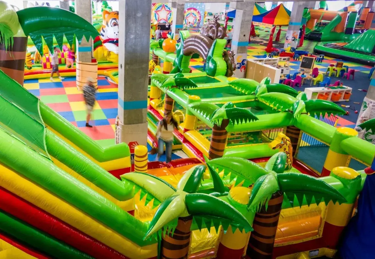 Kolorowy park rozrywki we Wrocławiu z dmuchanymi zjeżdżalniami i palmami. Dzieci biegają i bawią się w tropikalnym klimacie.