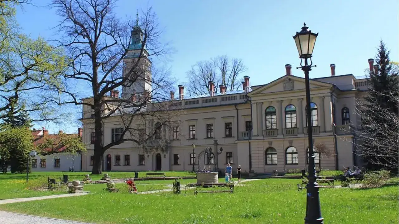 Piękny park w Żywcu z okazałym pałacem i wieżą. Wiosenna zieleń, ławki i zabytkowa latarnia tworzą urokliwą scenerię.