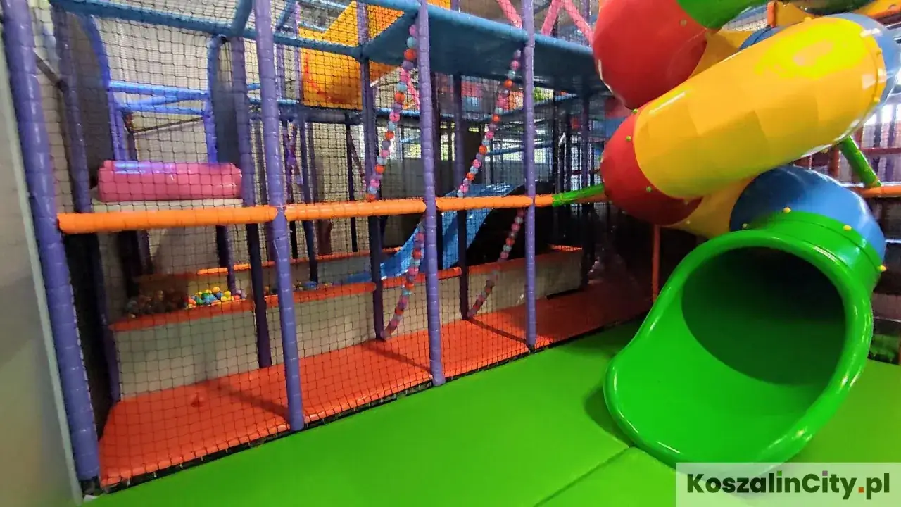 Kolorowy plac zabaw w parku rozrywki Koszalin z zieloną zjeżdżalnią, kulkami i wielopoziomowymi konstrukcjami.