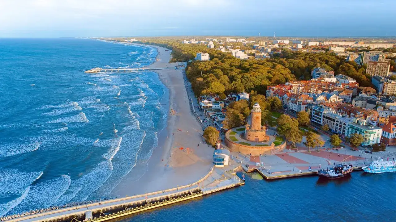 Widok z lotu ptaka na kołobrzeg plaża, z latarnią morską, molo i budynkami wzdłuż wybrzeża.