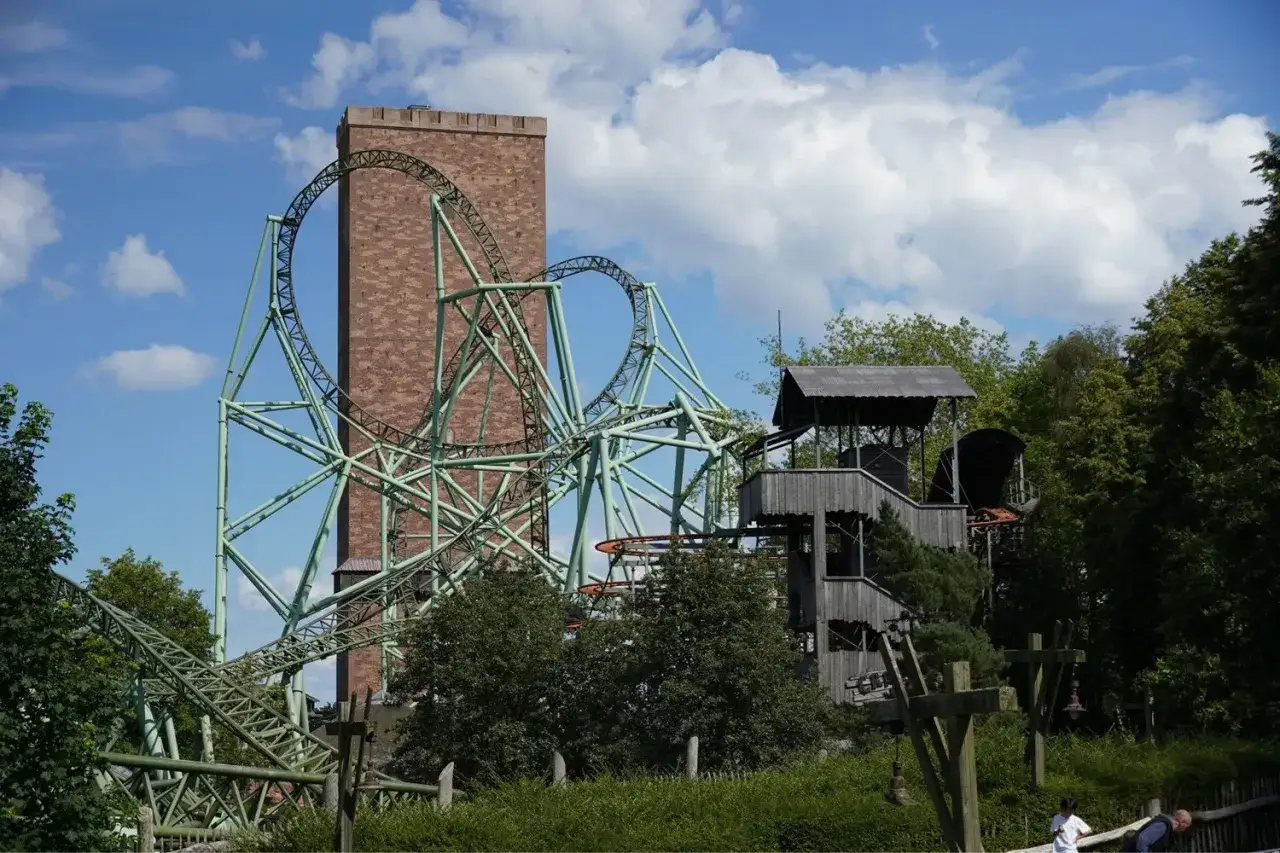 Zielona kolejka górska w parku rozrywki Hansa Park, z ceglaną wieżą w tle, zaprasza na ekscytującą przejażdżkę.