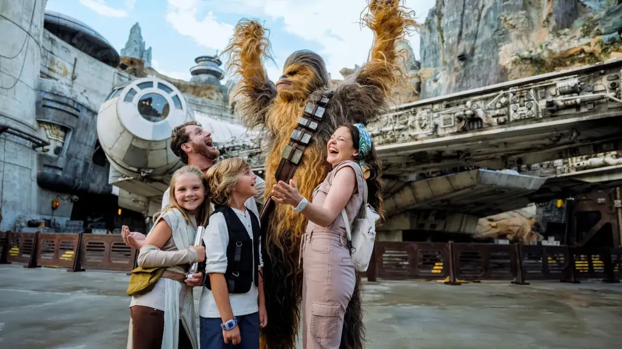 Rodzina śmieje się z Chewbaccą na tle Sokoła Millennium w Star Wars: Galaxy's Edge.