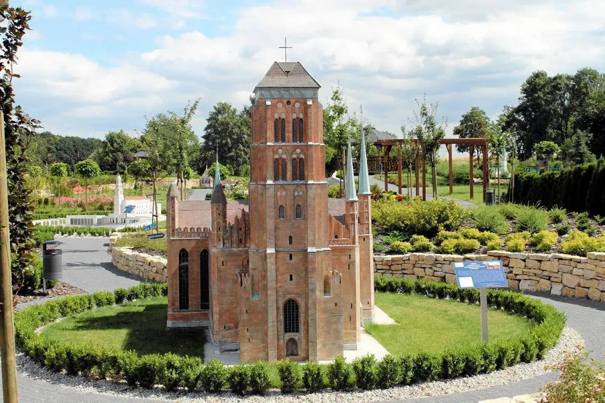 Miniaturowa katedra w parku miniatur sakralnych w Olszowej, otoczona zielenią i kamiennym murkiem.