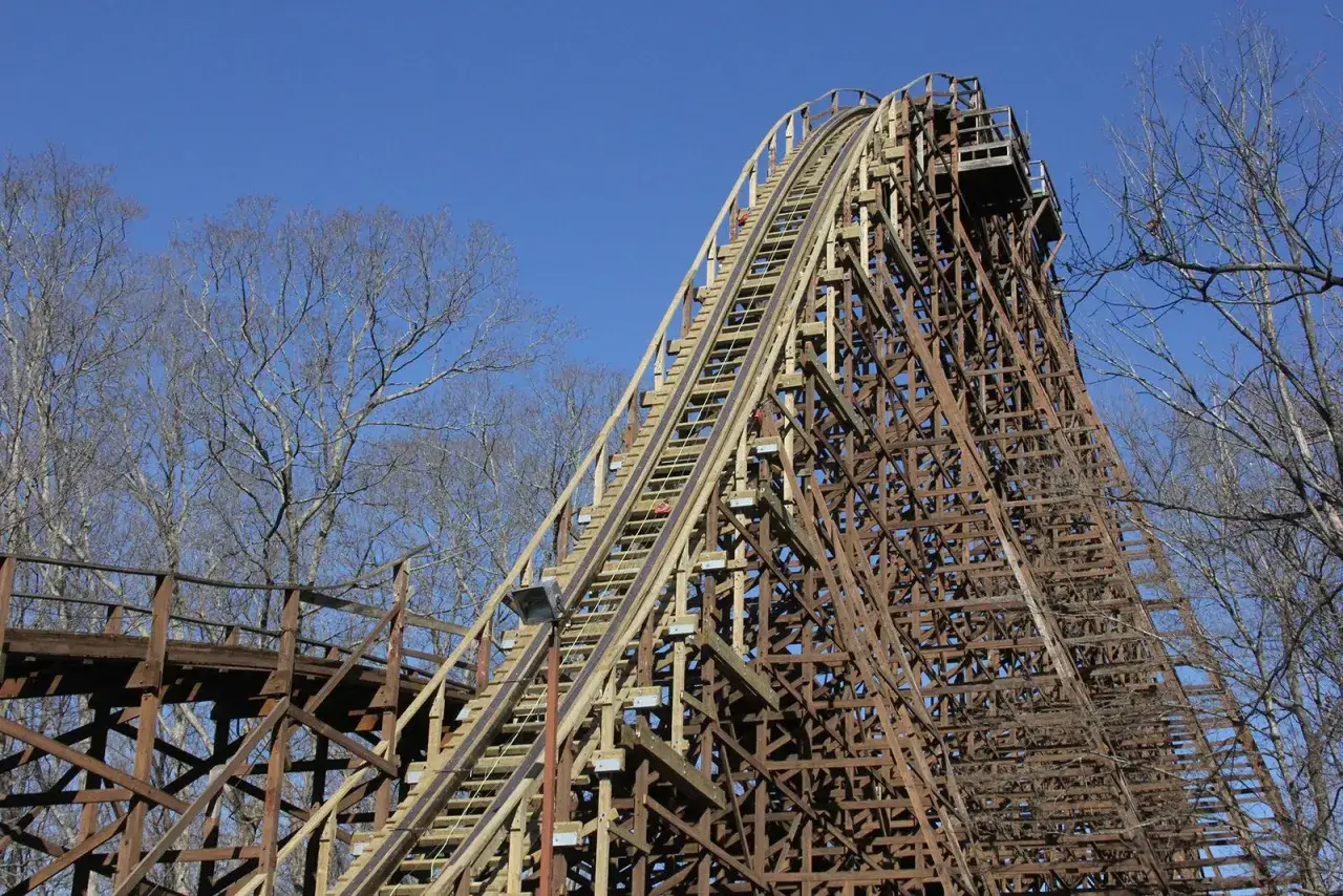 Imponujący, największy drewniany rollercoaster na świecie pnie się ku błękitnemu niebu, otoczony nagimi drzewami.