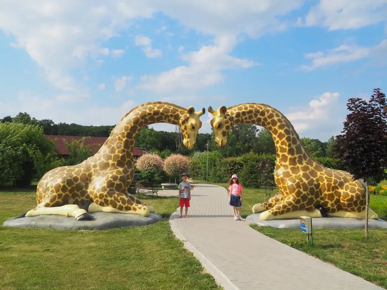 Dzieci pozują między gigantycznymi żyrafami w parku rozrywki Wielkopolska.