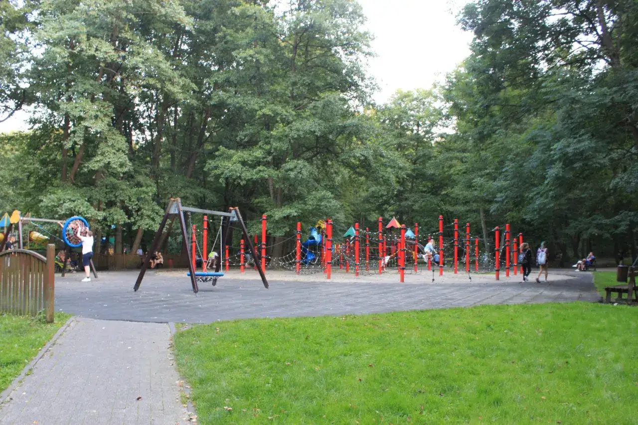Kolorowy plac zabaw w parku w Wejherowie z huśtawkami, zjeżdżalniami i ściankami wspinaczkowymi, otoczony zielenią.