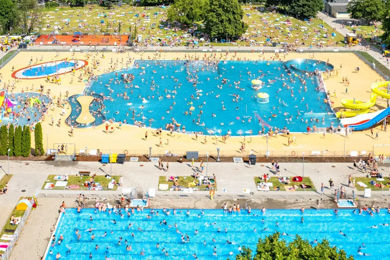 Tłum ludzi korzysta z atrakcji w moczydło park wodny. Woda w basenach jest turkusowa, a wokół leżą opalający się.
