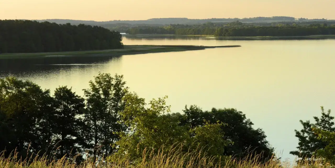 Zachód słońca nad jeziorem, otoczonym lasami. Idealne miejsce na mazury atrakcje, relaks i podziwianie natury.