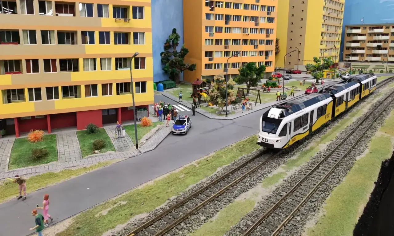 Miniaturowy pociąg KD mija osiedle z kolorowymi blokami, placem zabaw i radiowozem. To miniaturowy park Wrocław.