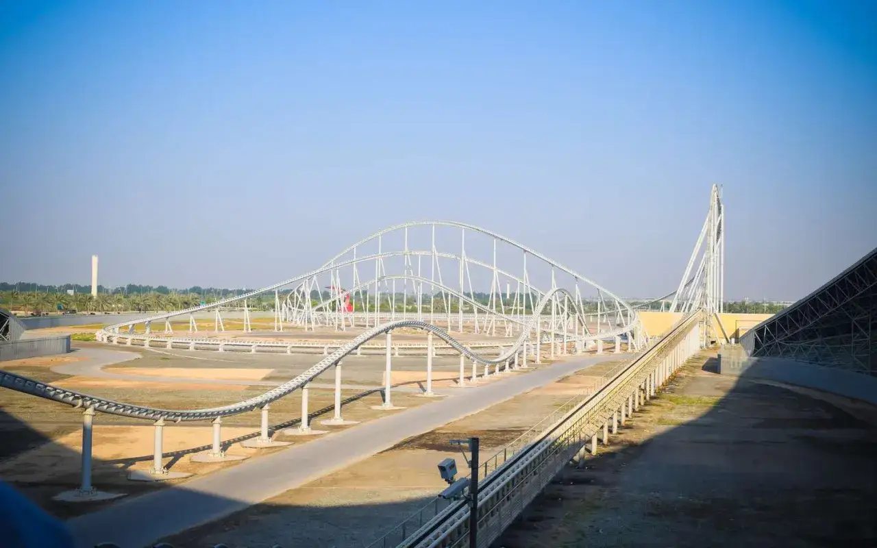 Biały, skomplikowany tor dla najszybszego rollercoastera na świecie, z palmami i budynkami w tle.
