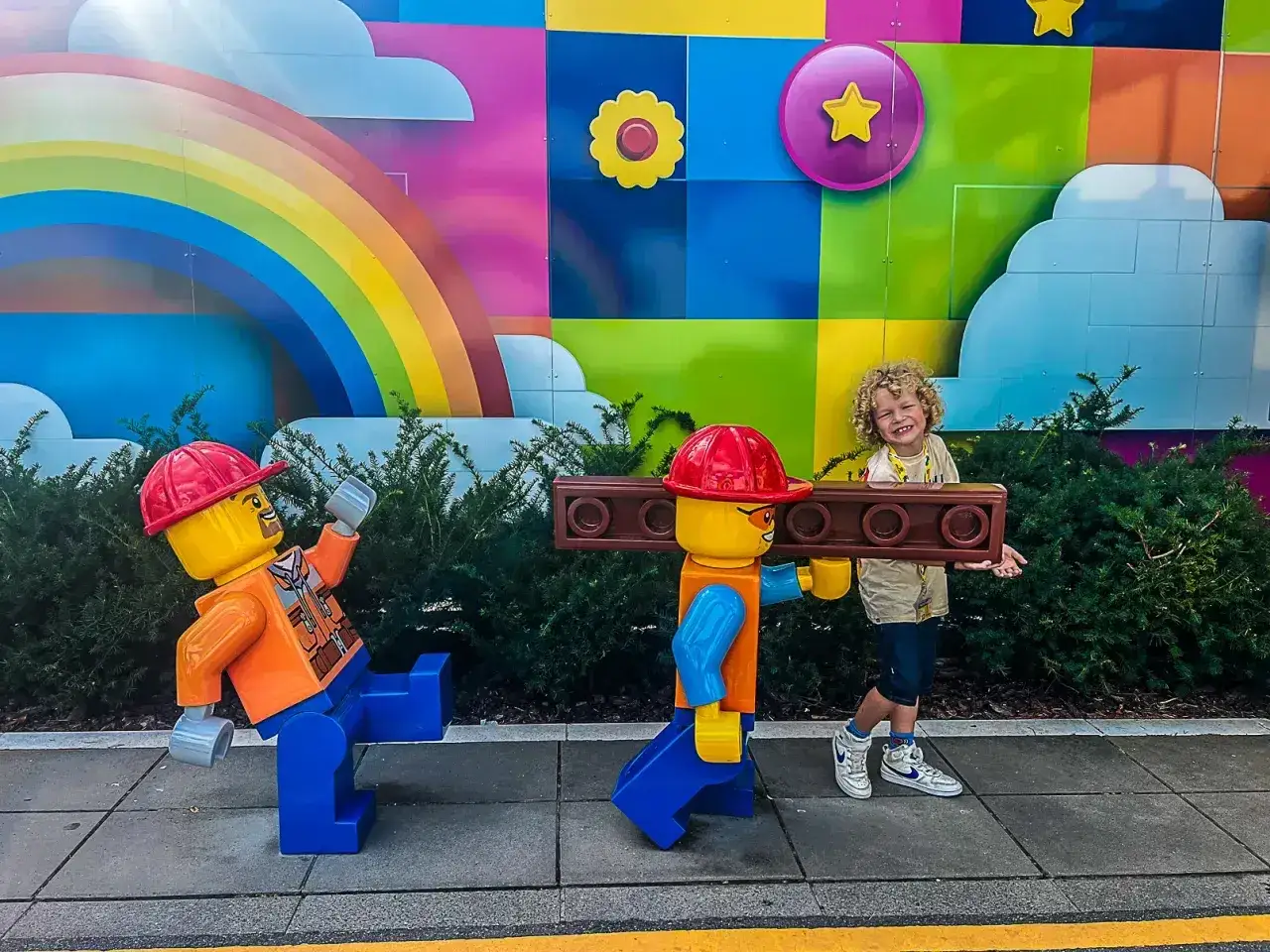 Chłopiec z uśmiechem na twarzy wśród gigantycznych klocków Lego. Kolorowa ściana z tęczą i chmurkami. Niezapomniane atrakcje Legoland Dania.