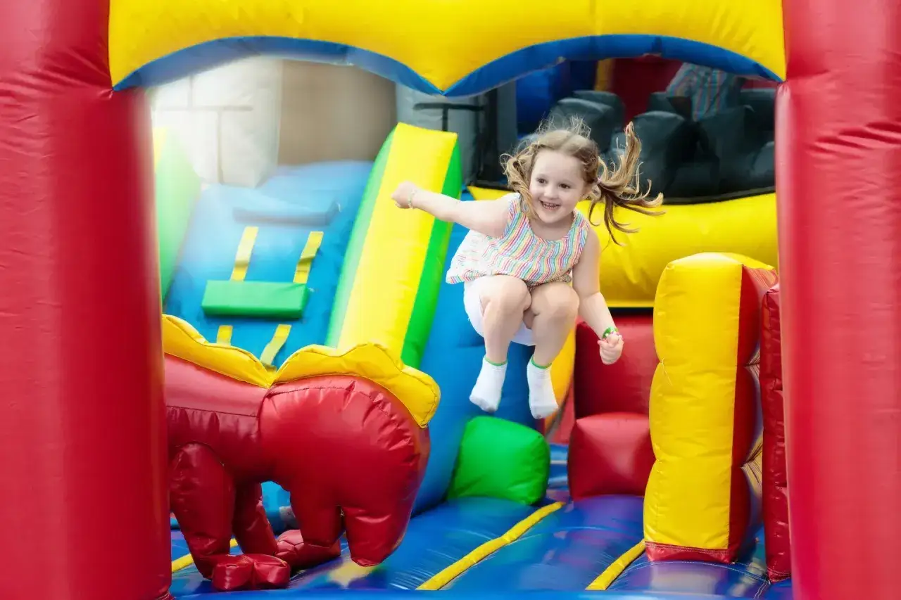 Radosna dziewczynka skacze na dmuchanym zamku w Ustronie Morskie Western Park. Kolorowa zjeżdżalnia i czerwony smok dodają zabawy.