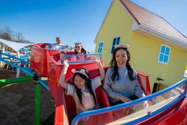 Rodzina cieszy się przejażdżką w Peppa Land Polska, z uśmiechniętymi dziećmi w uszkach świnki.
