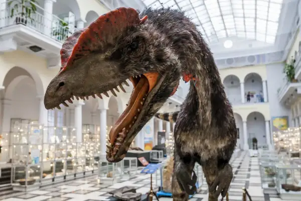 Model dinozaura z otwartym pyskiem w muzeum dla dzieci Warszawa. W tle gabloty z eksponatami i arkadowe galerie.