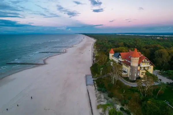 Zachód słońca nad jeziorem Łebsko i plażą. W oddali widać zalesione wybrzeże i malowniczy budynek z wieżą.