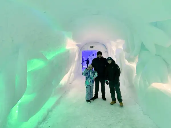 Rodzina w lodowym tunelu, gdzieś w okolicy wioski Mikołaja w Finlandii. Ściany lśnią zielonym światłem.