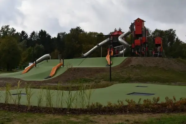 Nowoczesny lunapark w Łodzi z wieloma zjeżdżalniami, wieżami i trampolinami wbudowanymi w zielone wzgórza.