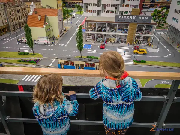 Dwie dziewczynki oglądają miniaturową ulicę z tramwajem i budynkami w parku miniatur Wrocław.