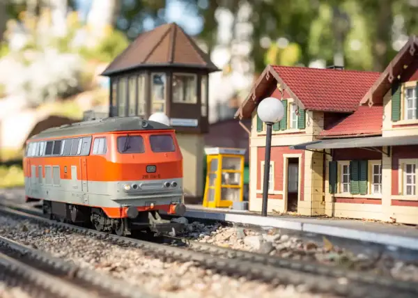 Miniaturowy pociąg na torach w parku miniatur i kolejek dziwnów. Stacja z budynkiem i budką telefoniczną.
