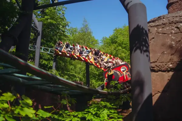 Pasażerowie na kolejce górskiej w kopenhaga park rozrywki, jadący przez zielony las.