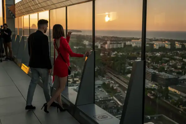 Para spaceruje po tarasie widokowym Olivia Star, podziwiając zachód słońca nad miastem i morzem.