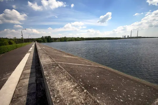 Droga biegnie wzdłuż betonowego muru nad spokojnym zalewem rybnickim. W oddali widać elektrownię.
