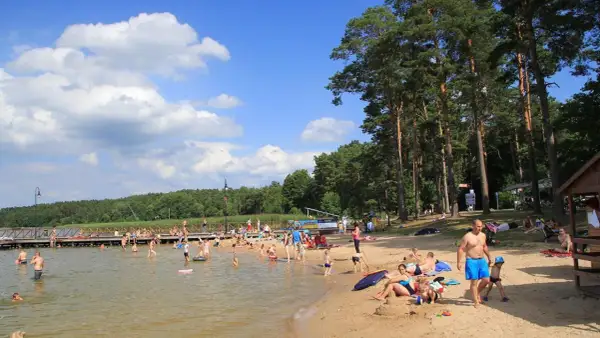 Słoneczna augustowska plaża tętni życiem. Ludzie kąpią się, opalają i relaksują na piasku, ciesząc się letnim dniem nad jeziorem.