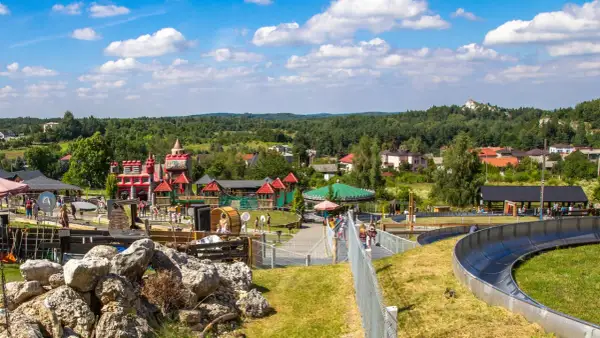 Kolorowy zamek i karuzela w **Ogrodzieńcu park rozrywki**. Dzieci bawią się na zjeżdżalni i placu zabaw.