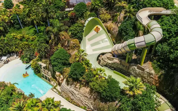 Ekscytująca zjeżdżalnia w Siam Park, z osobą na pontonie wpadającą do basenu. Wokół bujna roślinność.