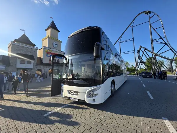 Biały autokar czeka na pasażerów przed wejściem do Energylandii. W tle widać zamek i kolejkę górską. To idealny pociąg do Energylandii!