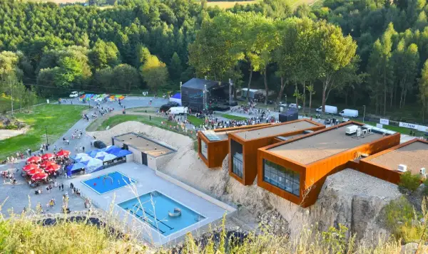Ulinapark tętni życiem: koncert na scenie, baseny, punkty gastronomiczne i nowoczesne budynki na skale.