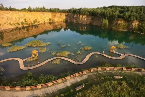 Malowniczy park Gródek z drewnianymi kładkami wijącymi się pośród turkusowej wody i wysepek z trzcinami.